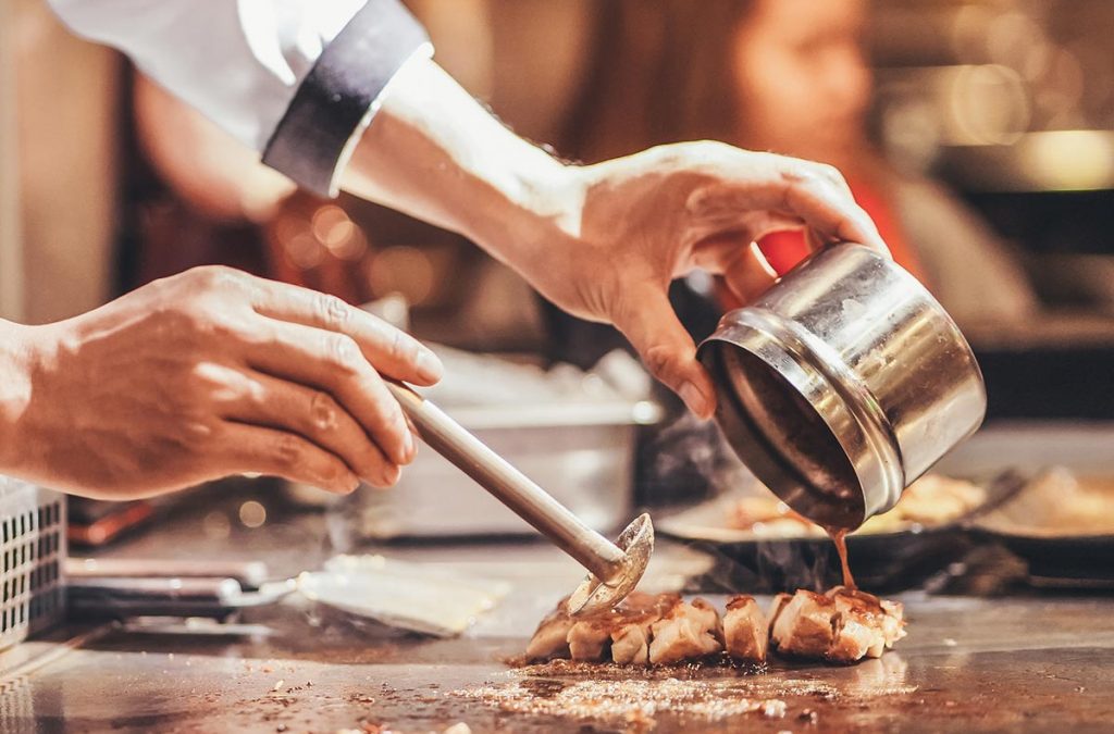 Chef adding a sauce to slices of pork.